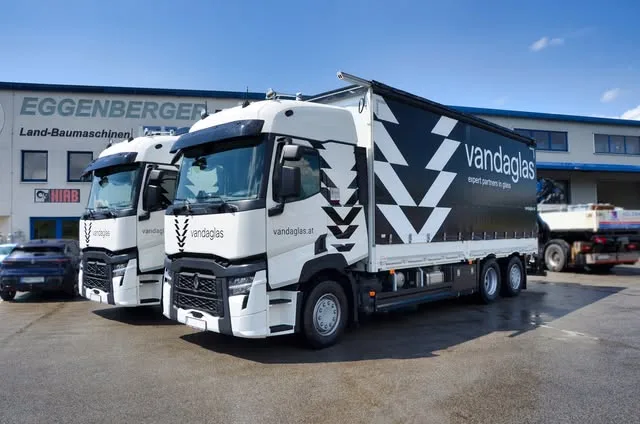 Zwei weiße Renault-LKW mit Planenaufbau vor der Halle mit dem Schriftzug Eggenberger