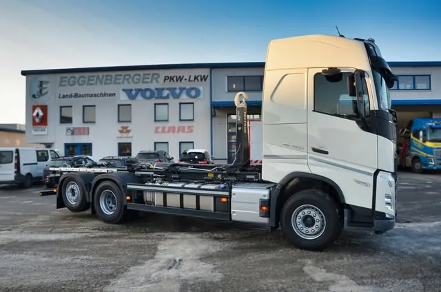 Volvo FH mit Hakenlift-Fahrgestell vor der Halle, an der Fassade die Schriftzüge Volvo und Claas